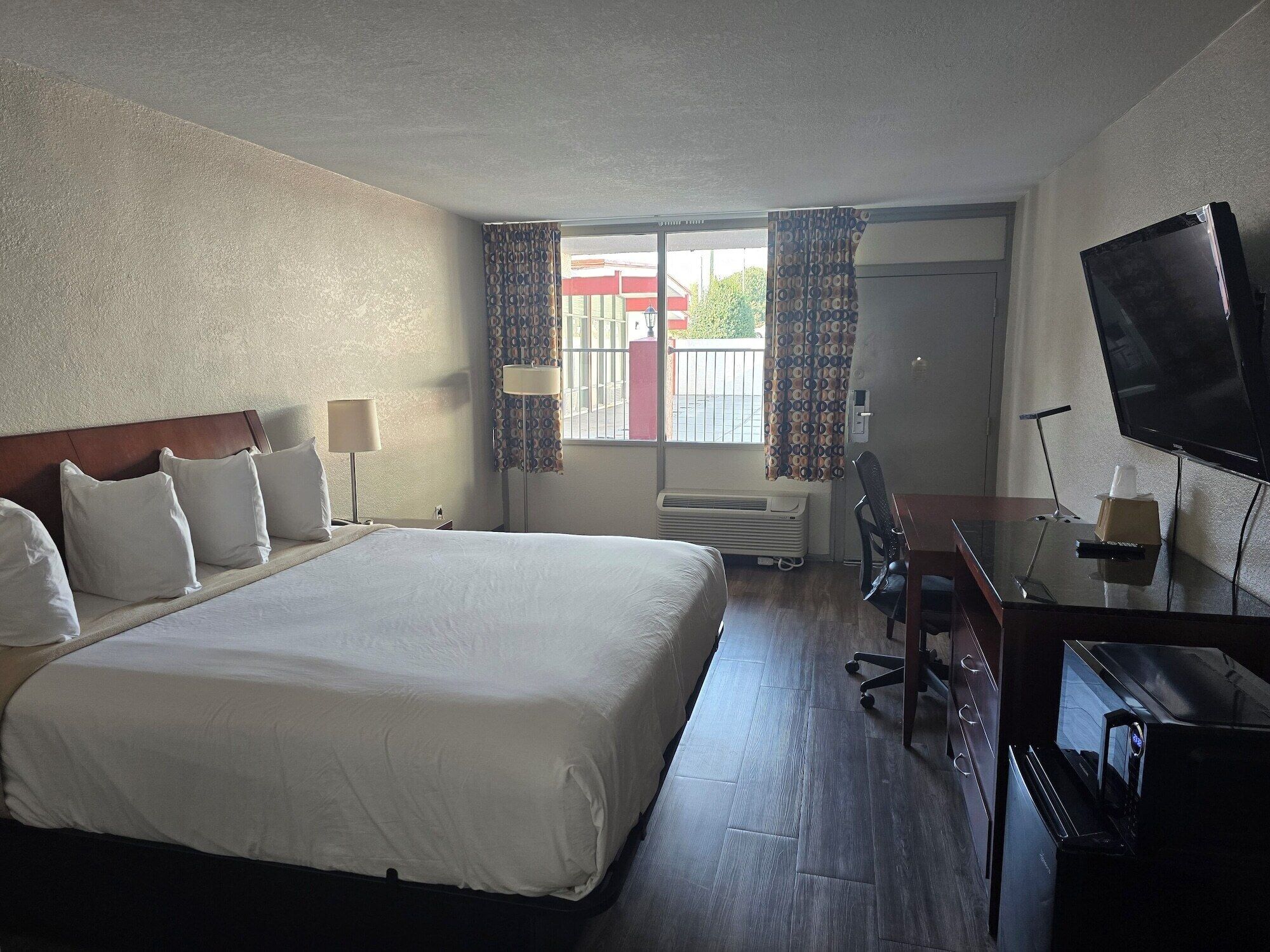 A hotel room with a large bed, a desk with a chair, a television, and a window with curtains.