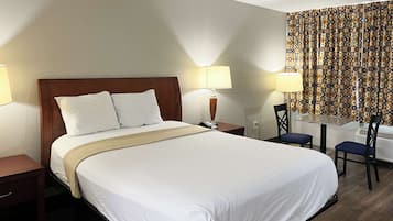 A hotel room with a large bed, two bedside tables, a desk with a chair, patterned curtains, and a window.
