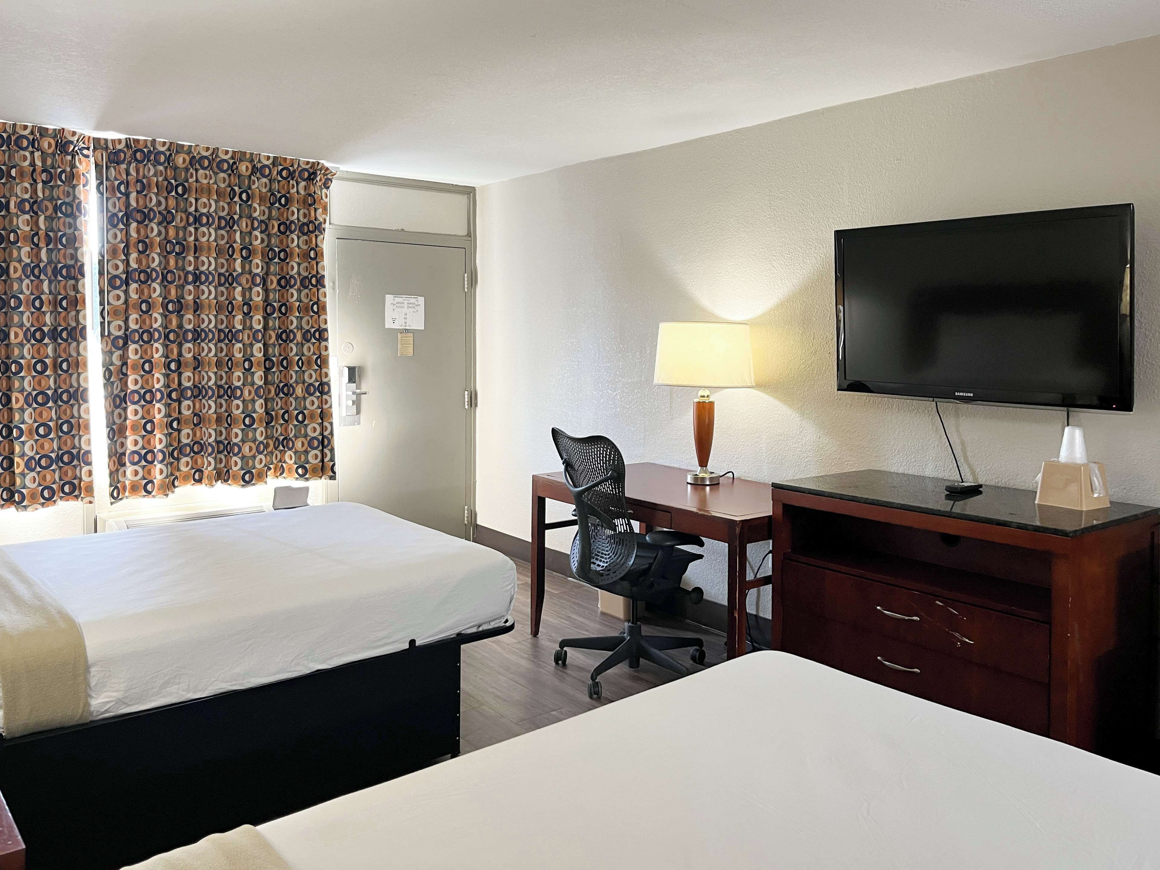 A hotel room with a bed, a desk with a chair, a television, and a lamp.