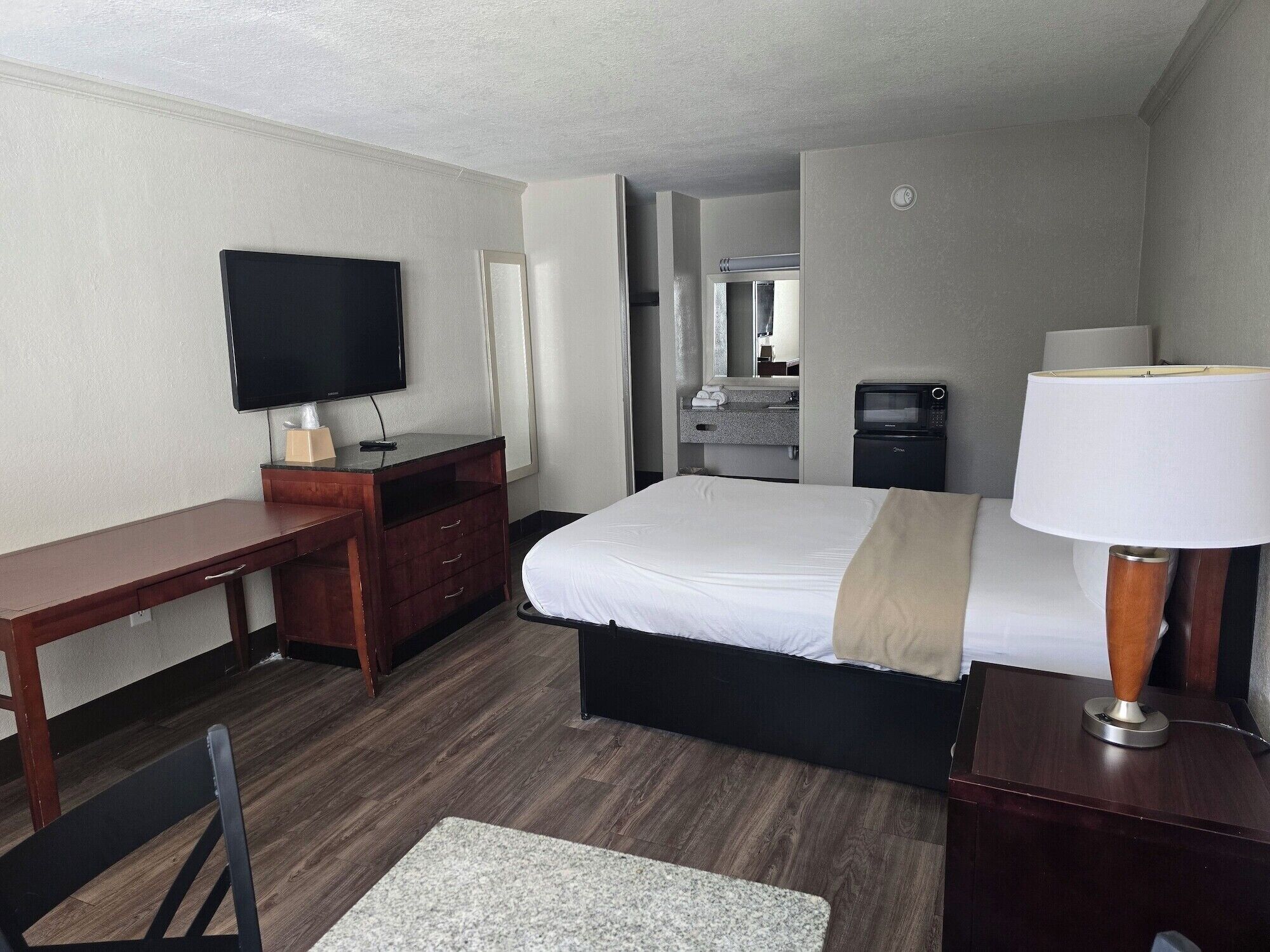 A hotel room with a bed, a desk, a television, a microwave, and a lamp.