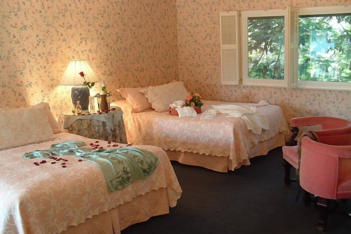 A room with two beds, a chair, a lamp, and a window with a view of trees.