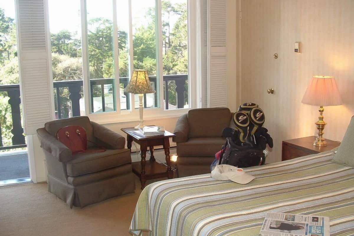 A bedroom with a bed, two armchairs, a small table, and a lamp.