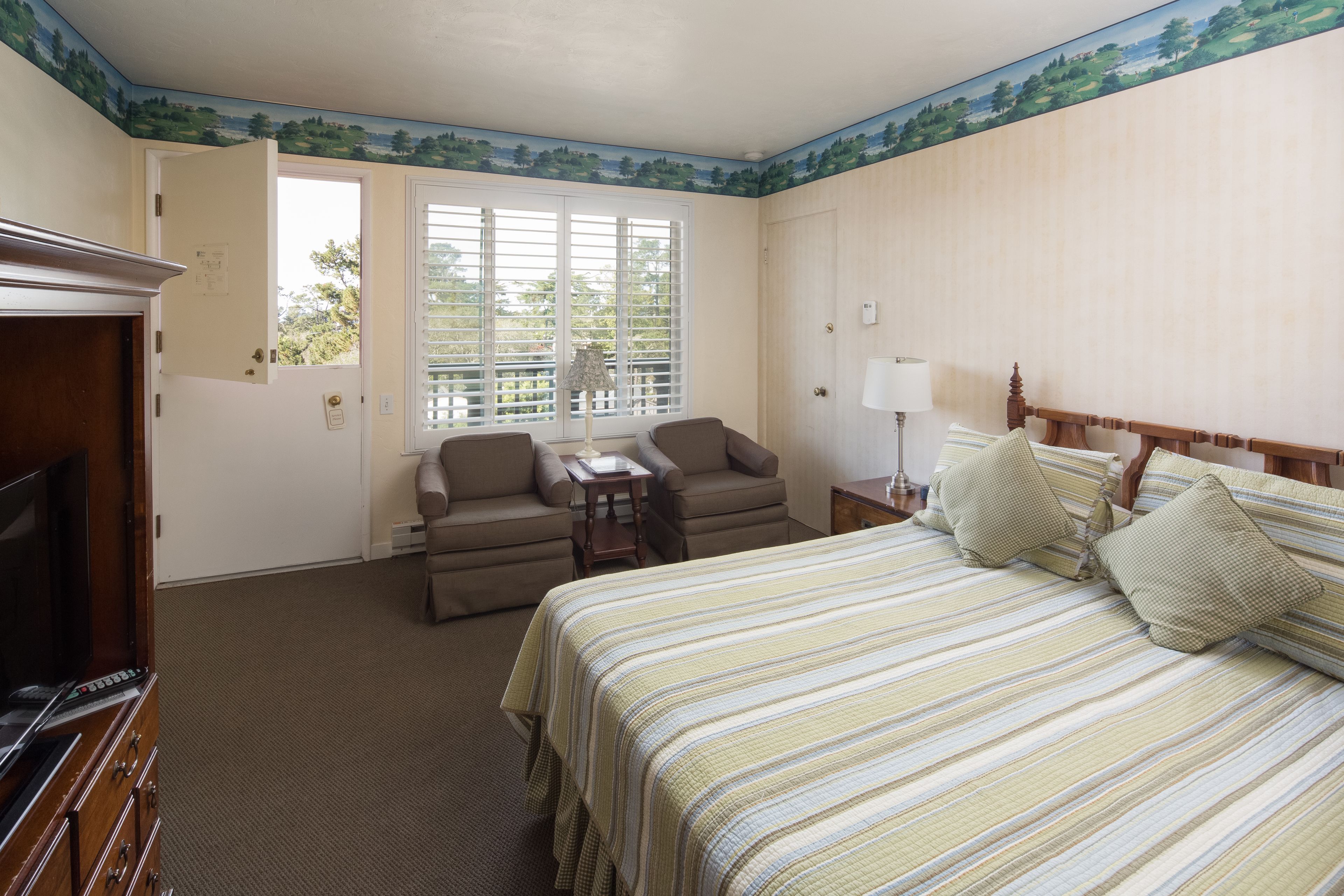 A hotel room with a bed, a television, a desk, and a window with blinds.