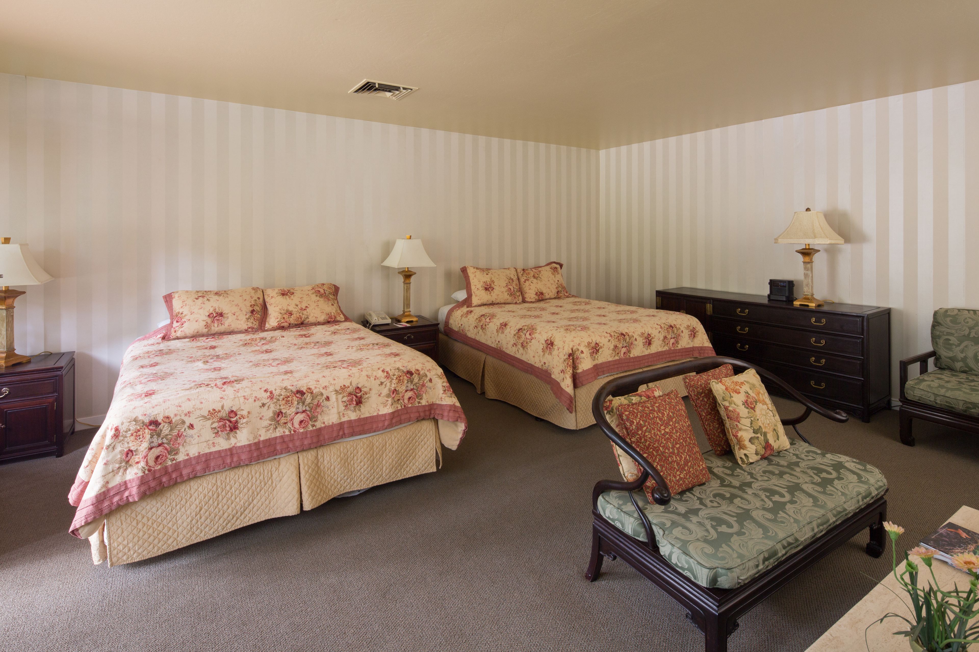 A hotel room with two beds, a nightstand, a dresser, a chair, and a lamp.