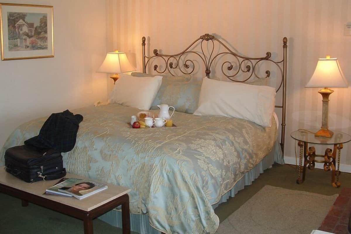 A neatly made bed with a decorative headboard, two bedside lamps, and a small table with a magazine and a suitcase.