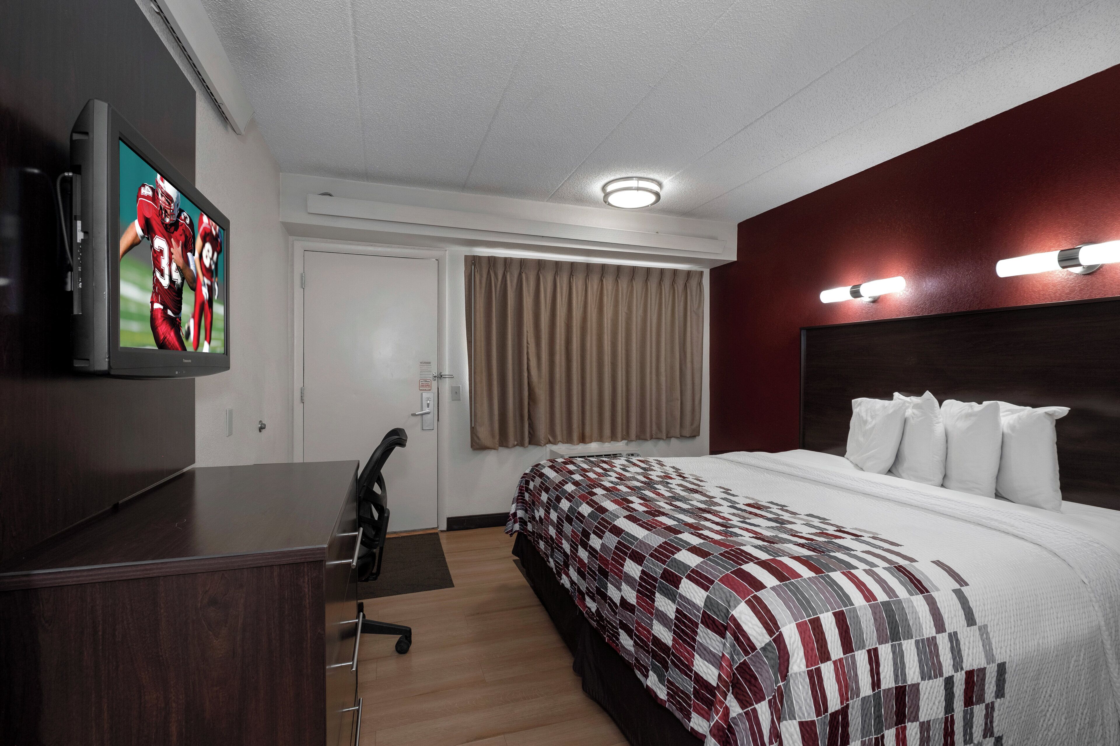 A hotel room with a bed, a desk, a television, a door, and a window with curtains.