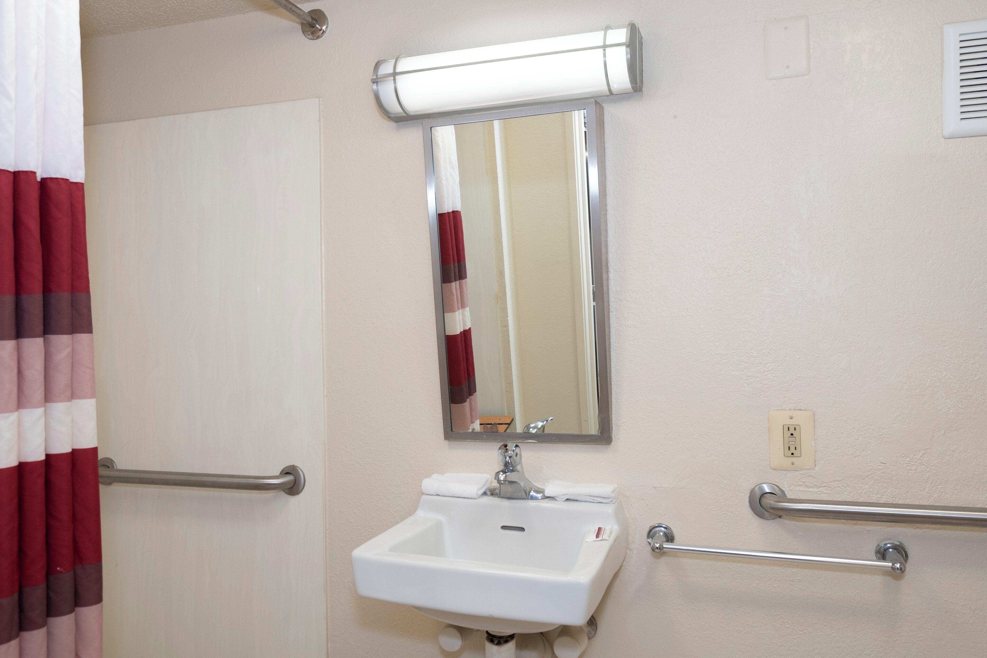 A bathroom with a white sink, a mirror, a towel rack, and a handrail.