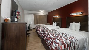 Ein Hotelzimmer mit zwei Betten, einem Schreibtisch, einem Fernseher und einem Fenster mit Vorhängen.