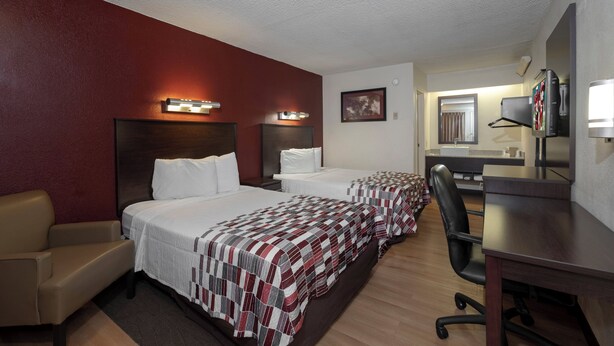 A hotel room with two beds, a desk, a chair, a TV, and a bathroom visible through an open door. - Red Roof Inn Washington DC - Lanham (Lanham)