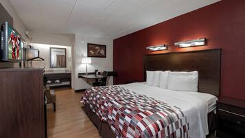 A hotel room with a large bed, a desk with a chair, a television, a mirror, and a red accent wall.