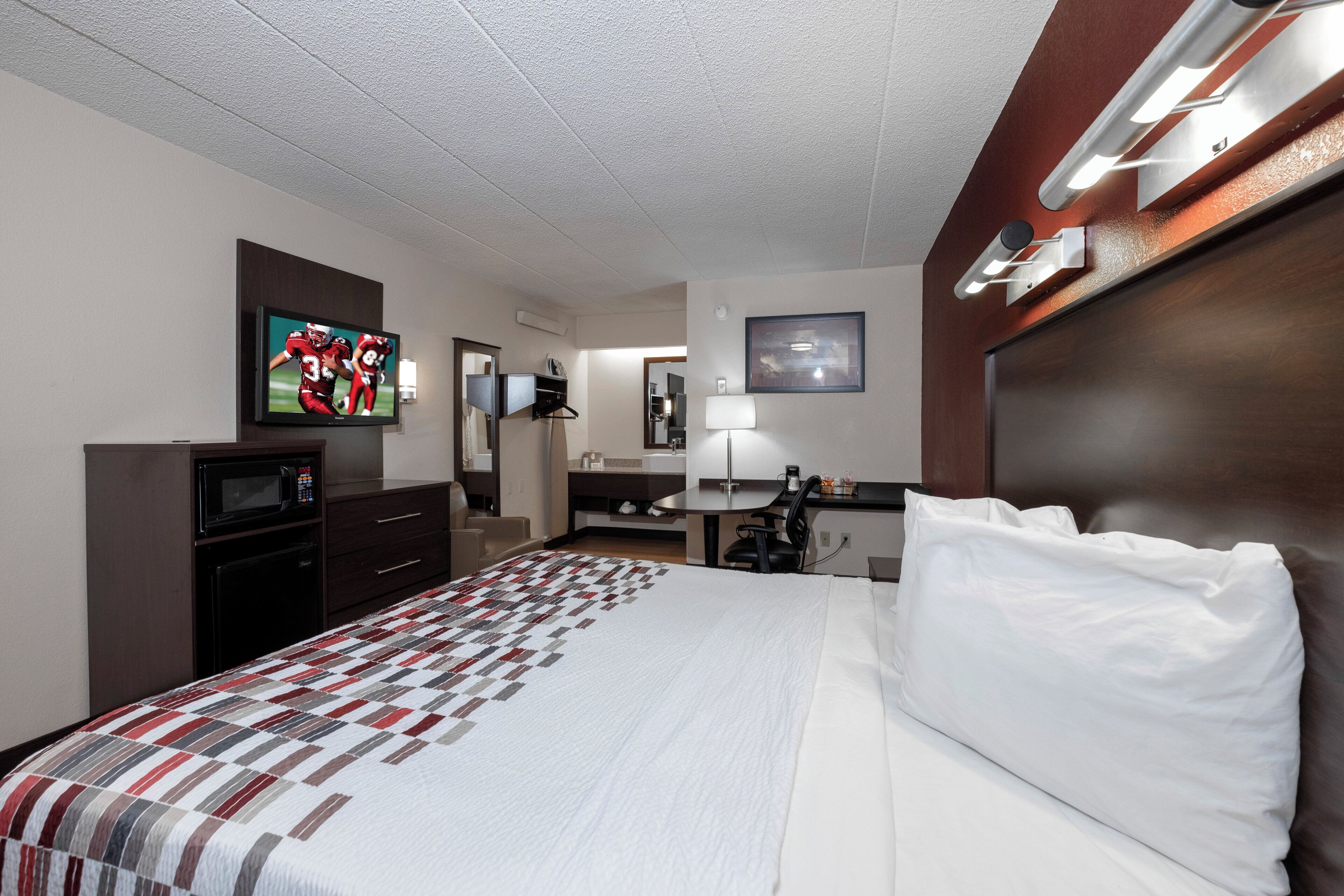 A hotel room with a bed, a TV, a desk, a chair, a microwave, and a coffee maker.
