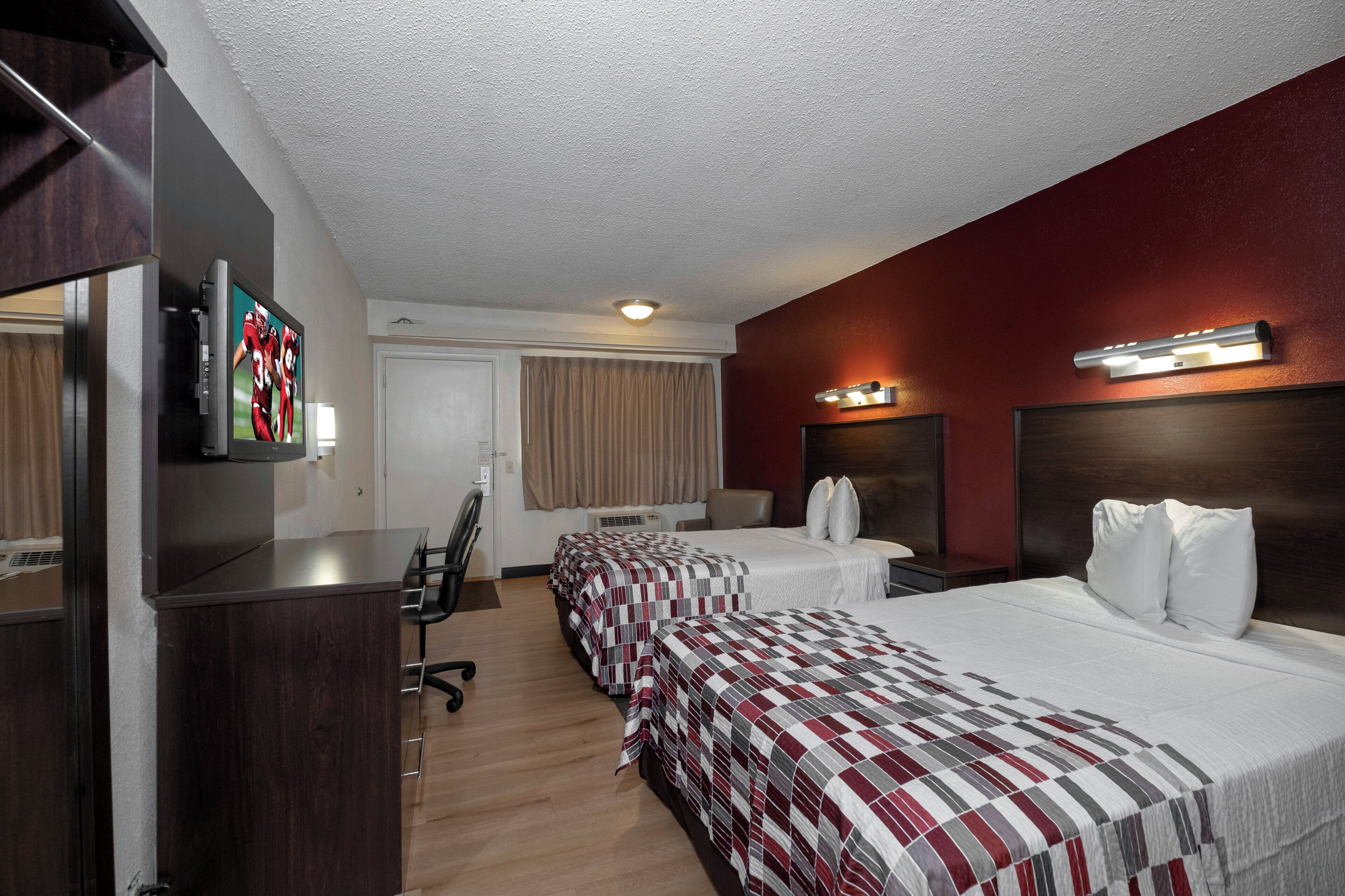 Habitación de hotel con dos camas, un escritorio, una silla, un televisor y una ventana con cortinas.