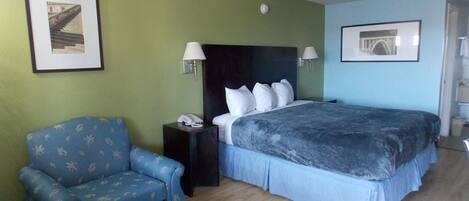 A hotel room with a bed, a chair, two wall lamps, and framed pictures on the walls.