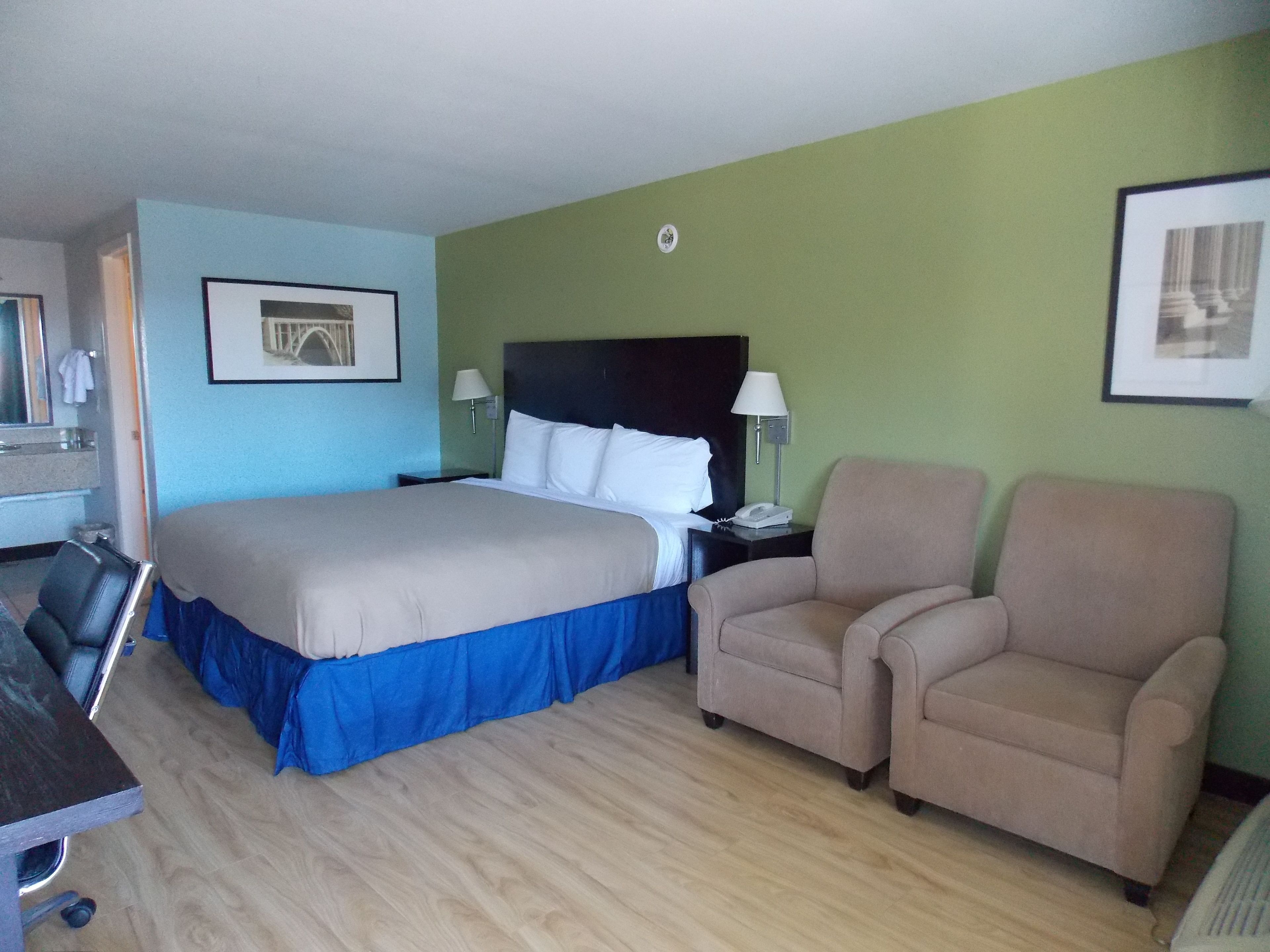 Una habitación de hotel con una cama grande, dos sillones, un escritorio y un espejo.