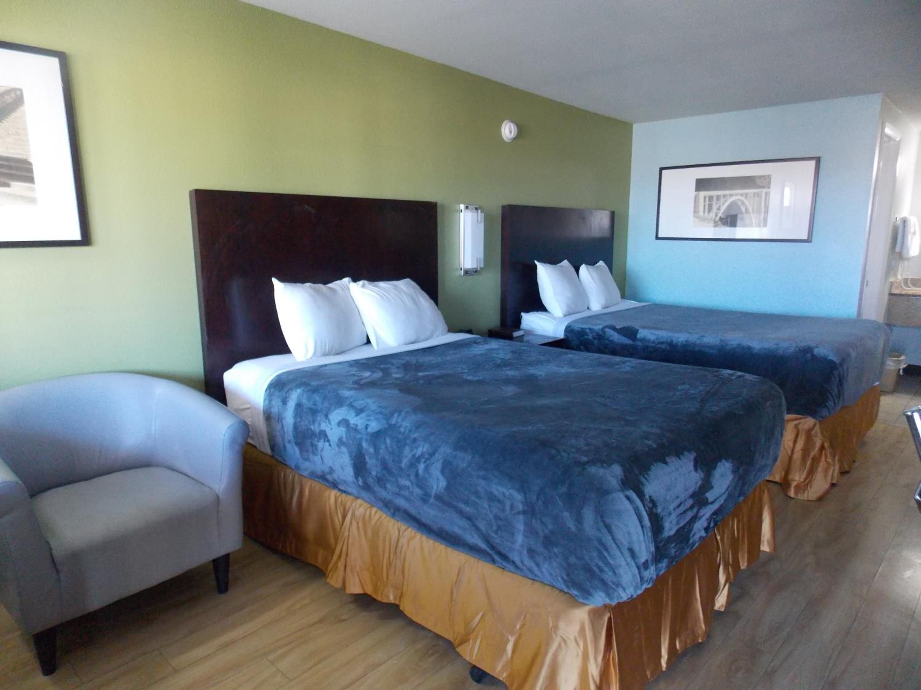 Una habitación de hotel con dos camas, una silla y un cuadro en la pared.