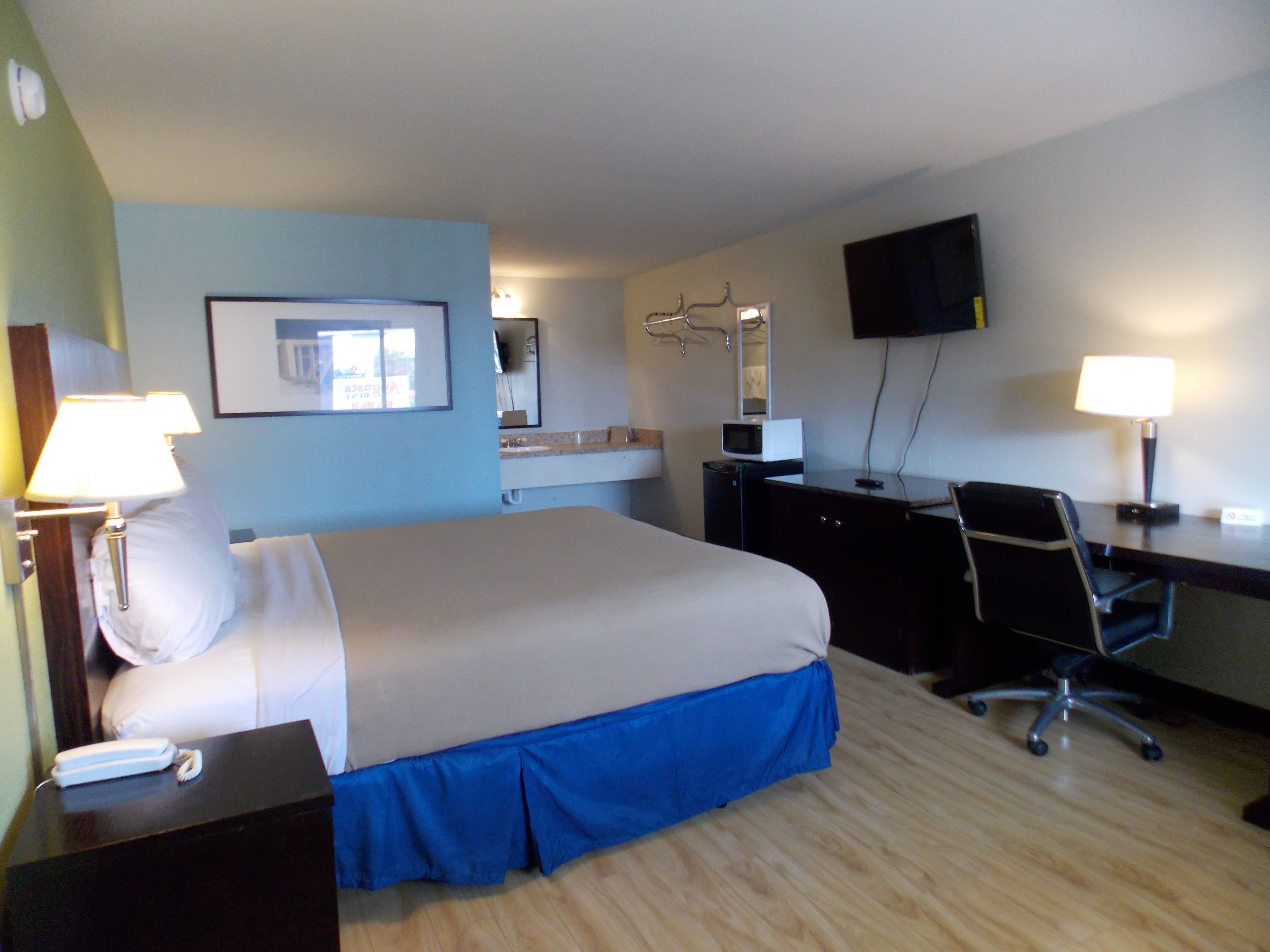 A hotel room with a bed, desk, chair, and a TV on the wall.