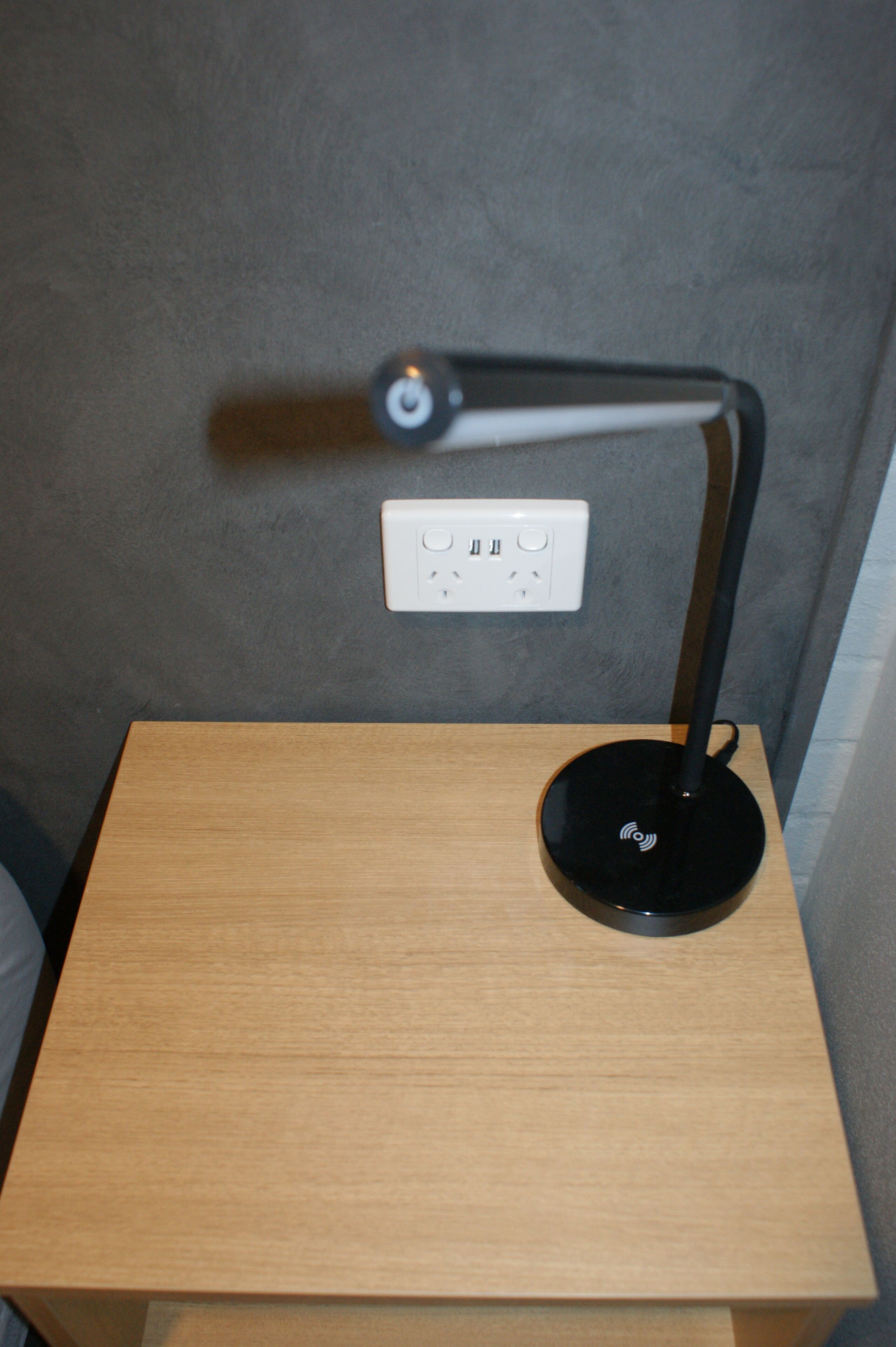 A small wooden table with a black desk lamp and a power outlet on the wall.