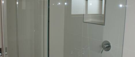 A glass-enclosed shower with a white towel hanging on the door, a mirror above the sink, and a wooden vanity.