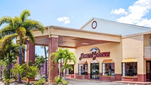 A Howard Johnson hotel with a covered entrance, palm trees, and a clear sky.