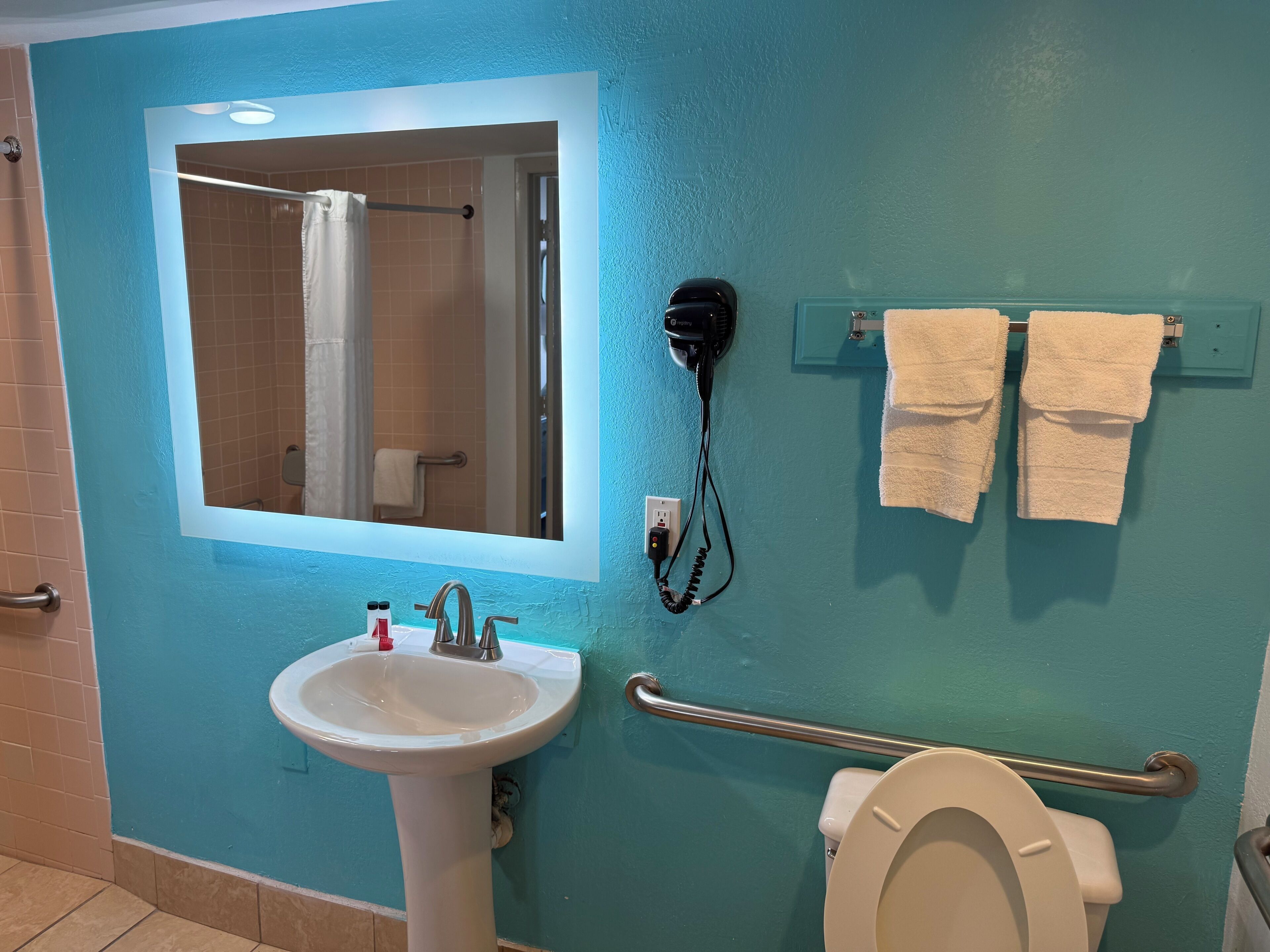 Un baño con lavamanos, espejo, secador de pelo, toallero y retrete.