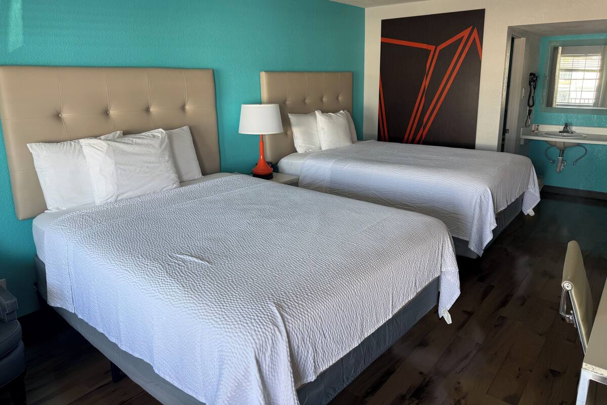 Hotelkamer met twee bedden, een nachtkastje met lamp, een badkamer met wastafel en spiegel, en een muur met geometrische kunstwerken.