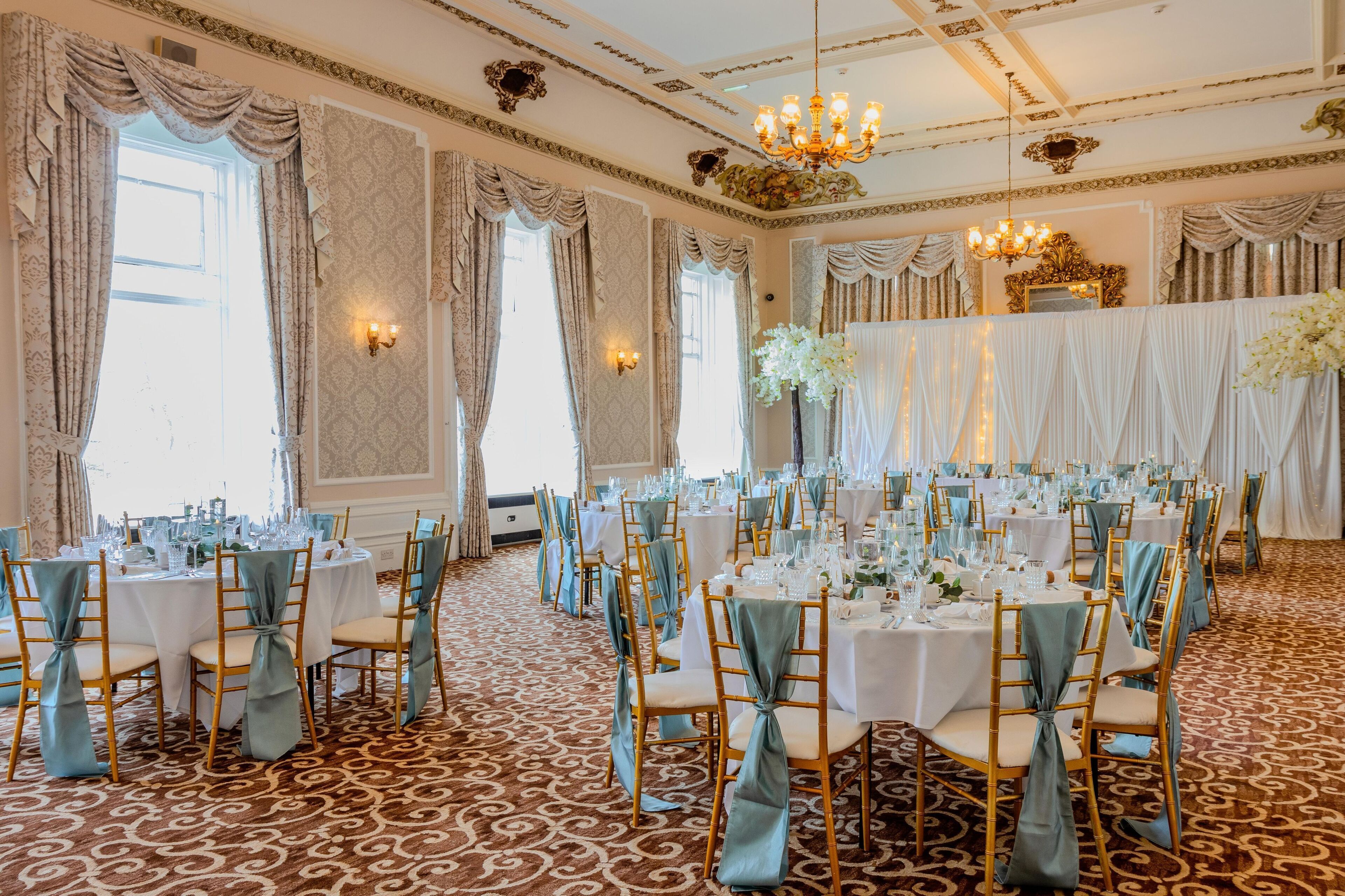 A banquet hall with round tables, chairs, and a patterned carpet.