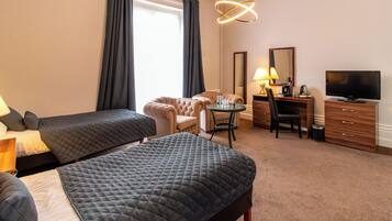 A hotel room with two beds, a desk, a chair, a television, and a lamp.