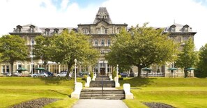 Stately hotel with a classic facade, surrounded by well-manicured lawns and trees, offering a serene setting.