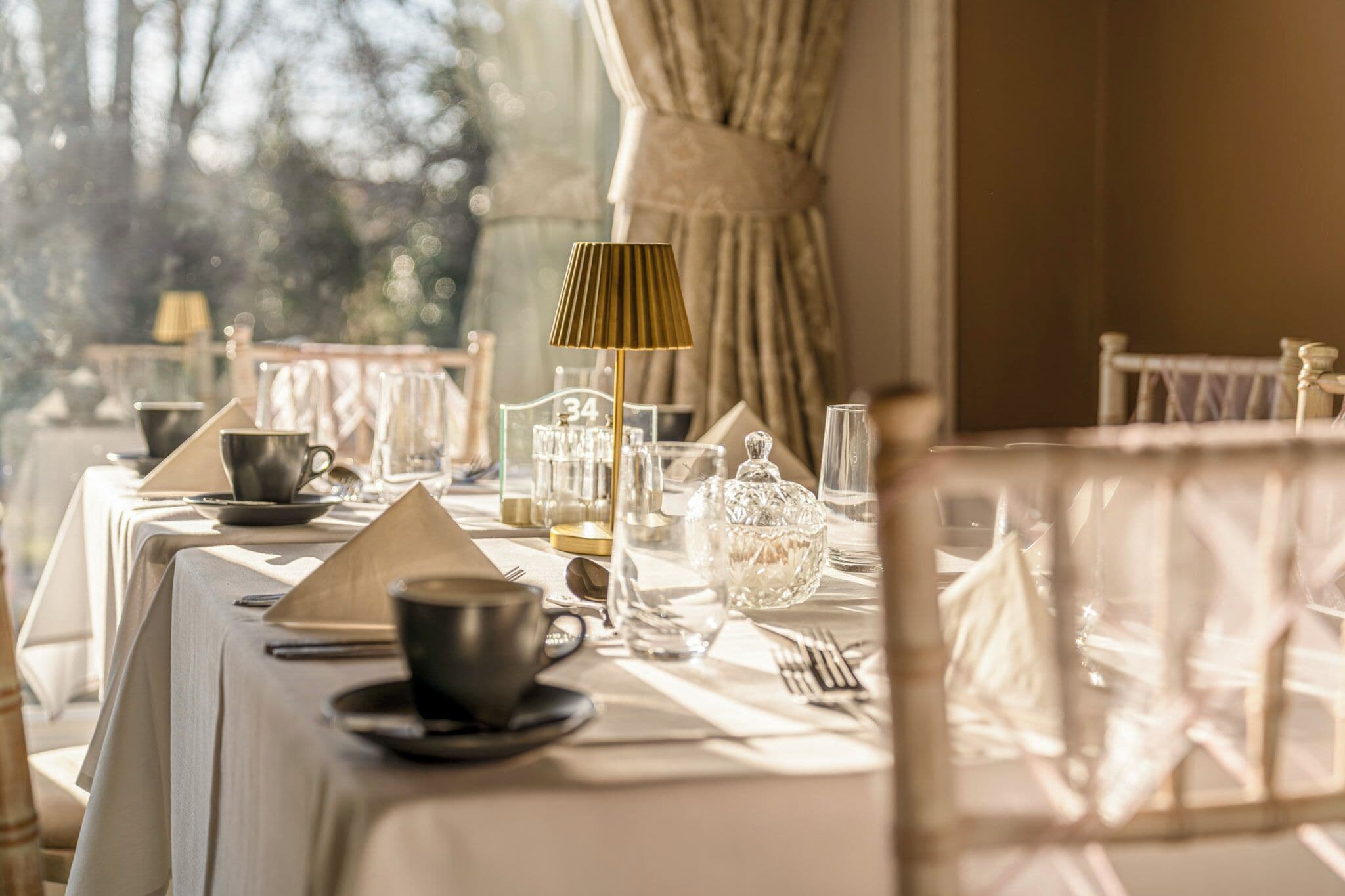 A dining table set with a candle, glassware, and a lamp.