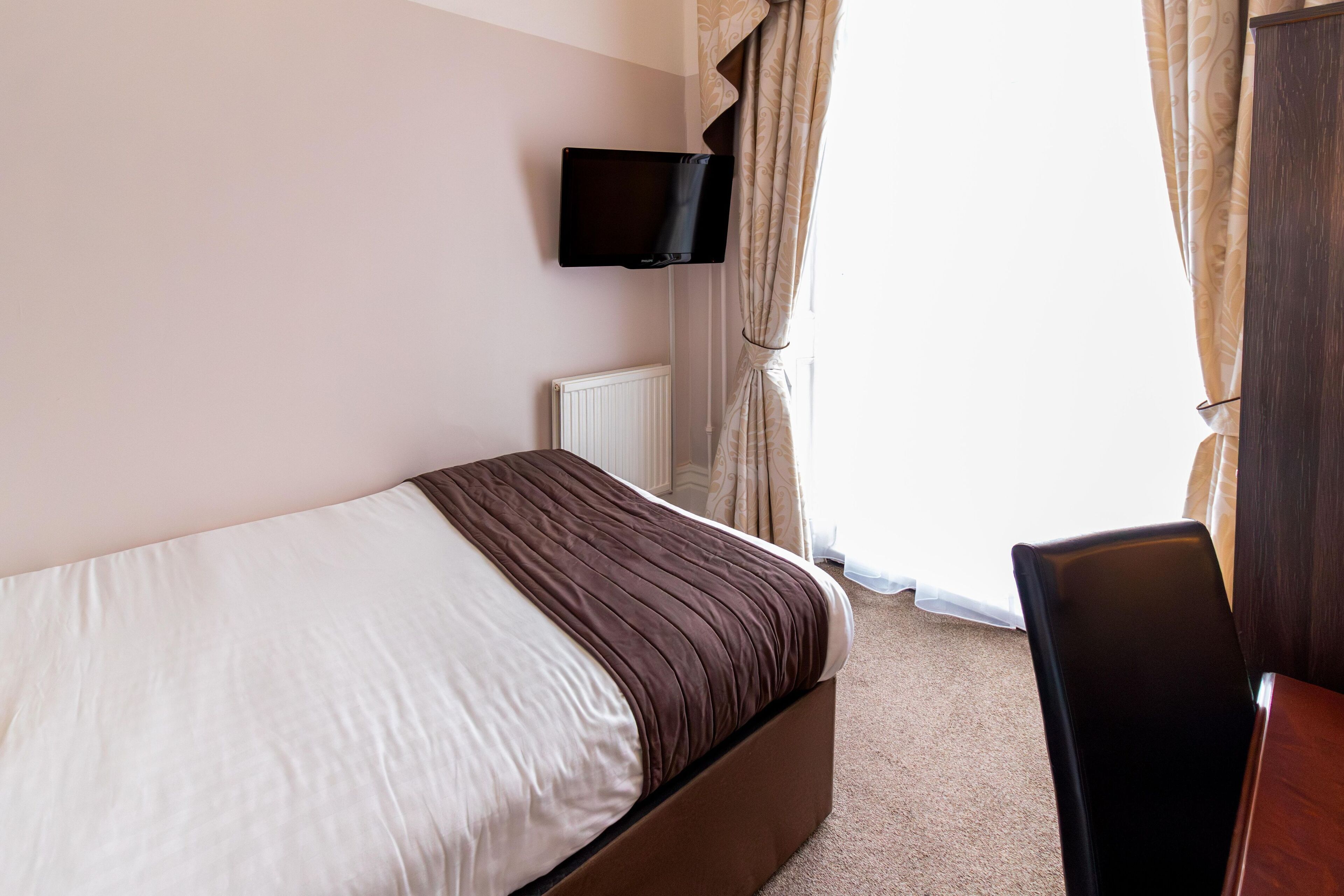 A hotel room with a bed, a flat-screen TV mounted on the wall, a chair, and a window with curtains.