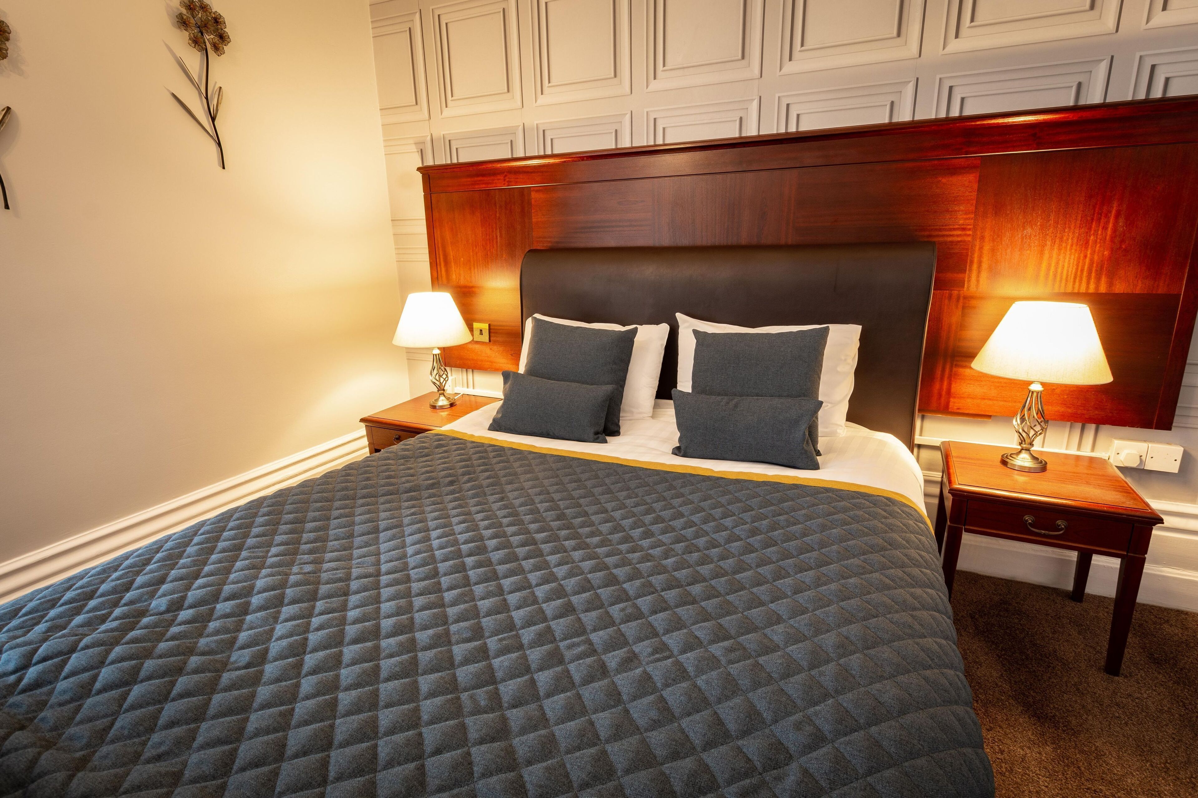 A neatly made bed with a quilted cover, two bedside tables with lamps, and a wooden headboard.