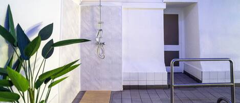A modern shower area with a handheld showerhead, a bench, and a potted plant.