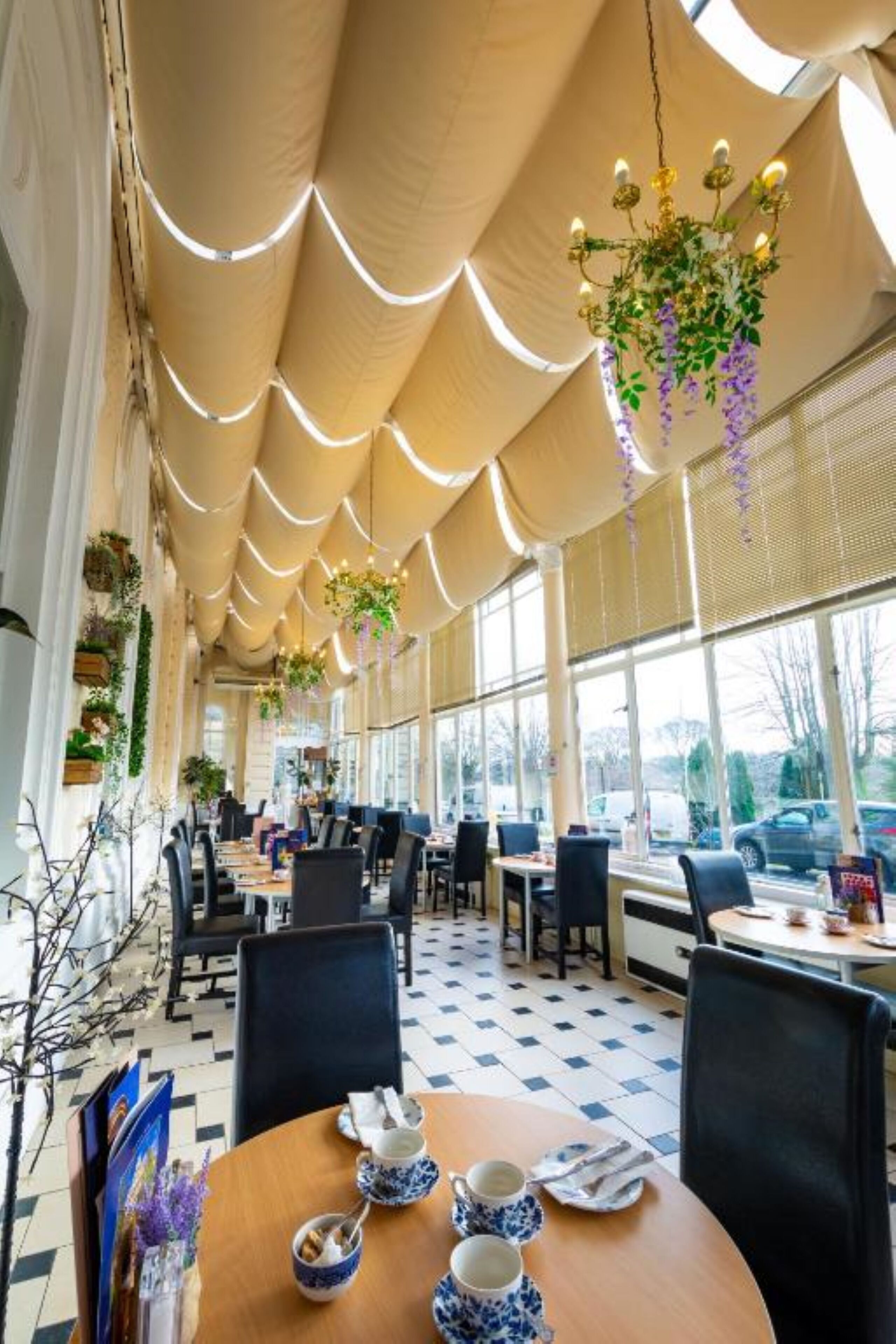A restaurant with a high ceiling, hanging plants, and a checkered floor. Tables are set with blue and white tableware.