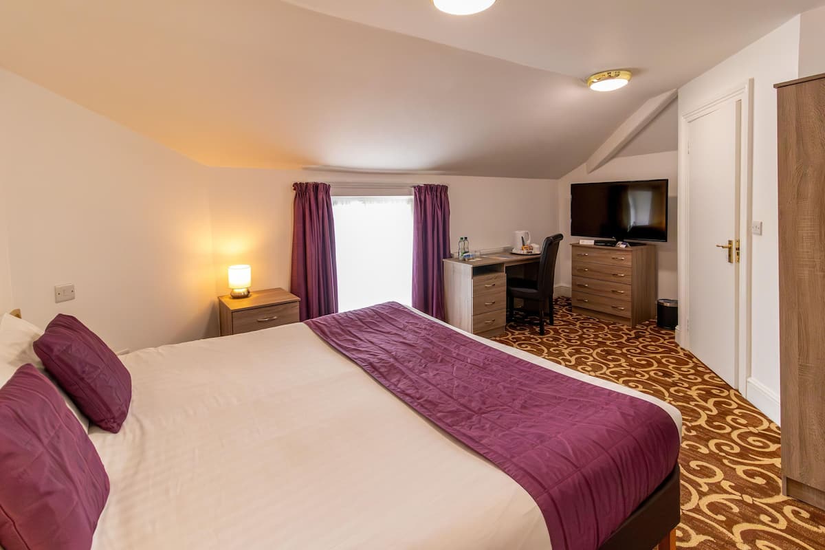 Ein Hotelzimmer mit Bett, Schreibtisch mit Fernseher, Kleiderschrank und Teppich mit Muster.