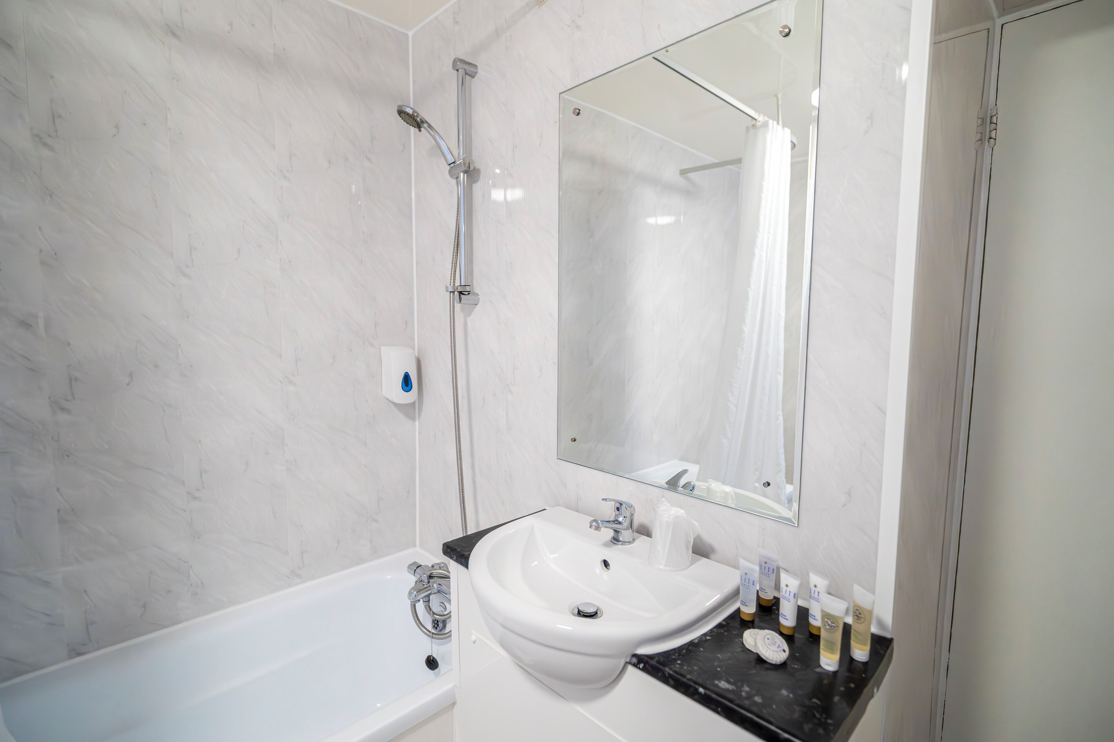 A modern bathroom with a white bathtub, a sink with toiletries, and a mirror.