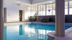 Una piscina interior con agua azul cristalina, rodeada de paredes blancas y amplias ventanas.
