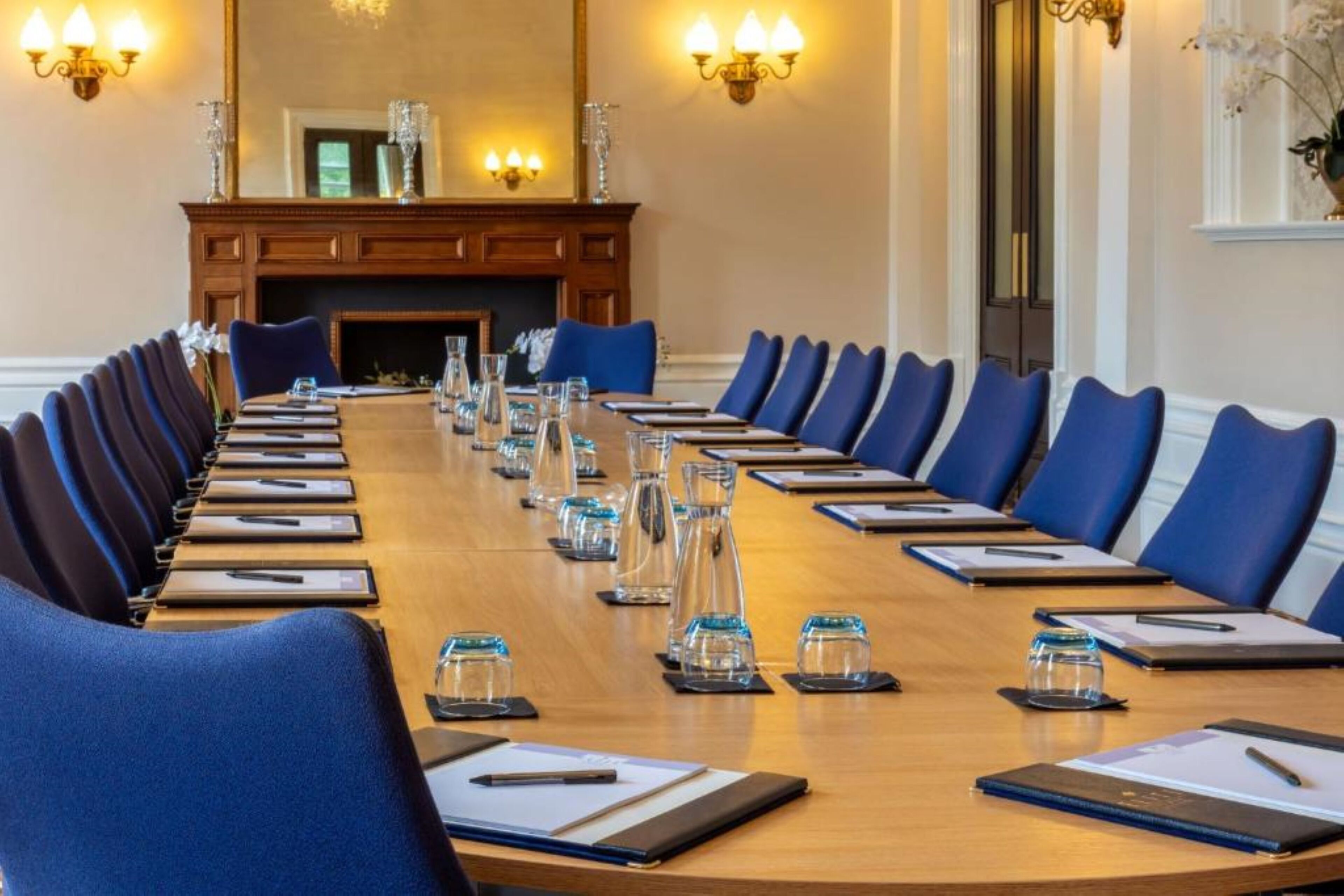 A conference room with a long table, blue chairs, and a fireplace.