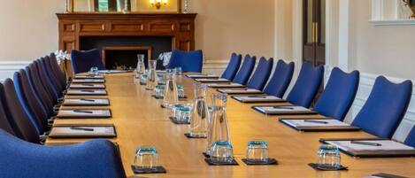 A conference room with a long table, blue chairs, and a fireplace.