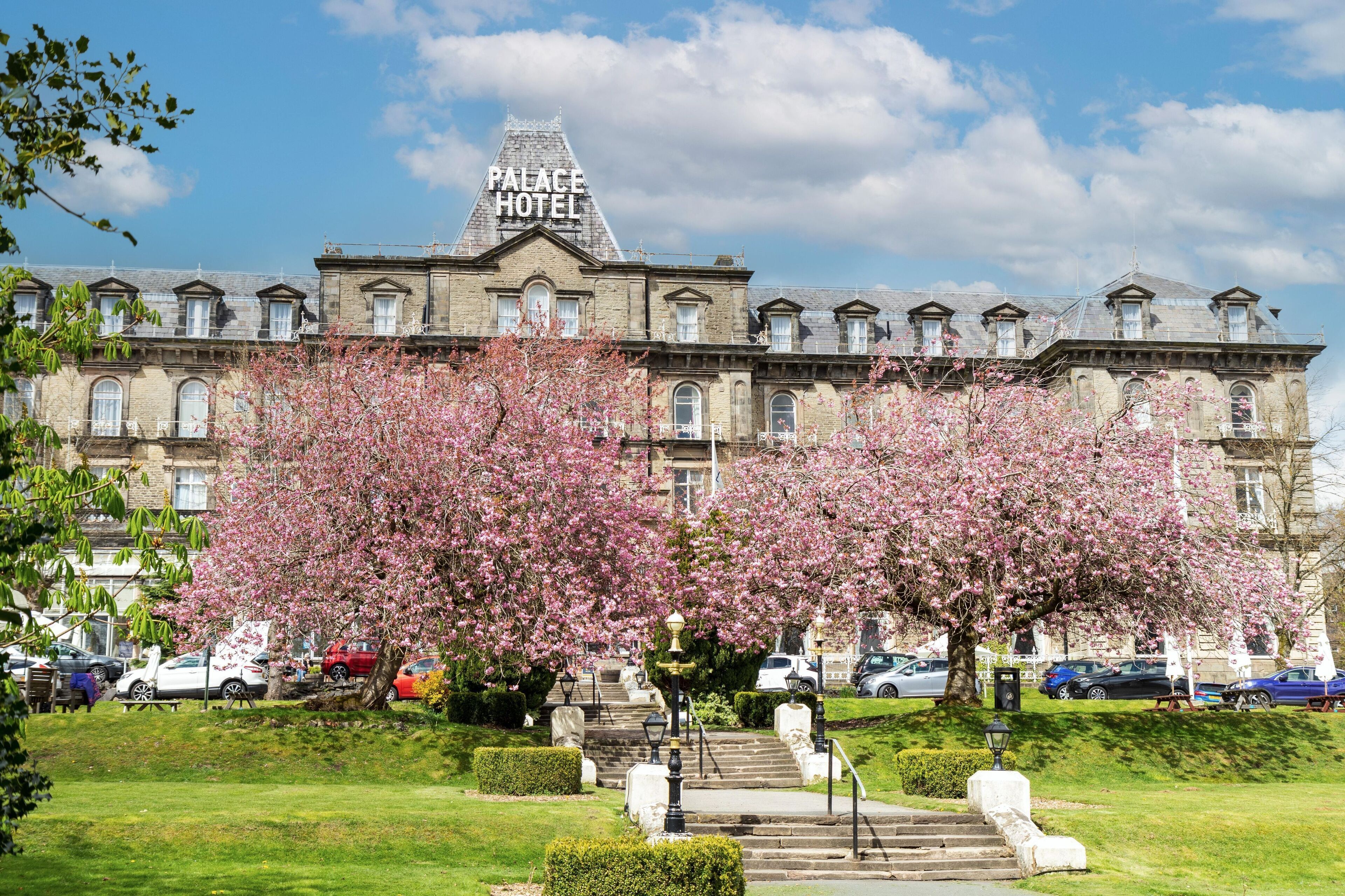 A historic building with a sign reading "Palace Hotel," surrounded by blooming cherry trees and a well-maintained lawn.