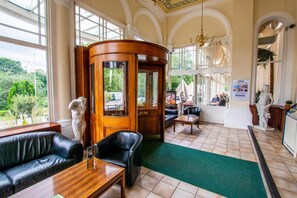 Experience the classic charm of our lobby, featuring a curved reception desk, comfortable seating areas, and stunning views of lush greenery.
