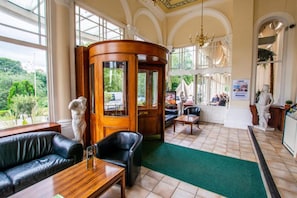 Experience the classic charm of our lobby, featuring a curved reception desk, comfortable seating areas, and stunning views of lush greenery.