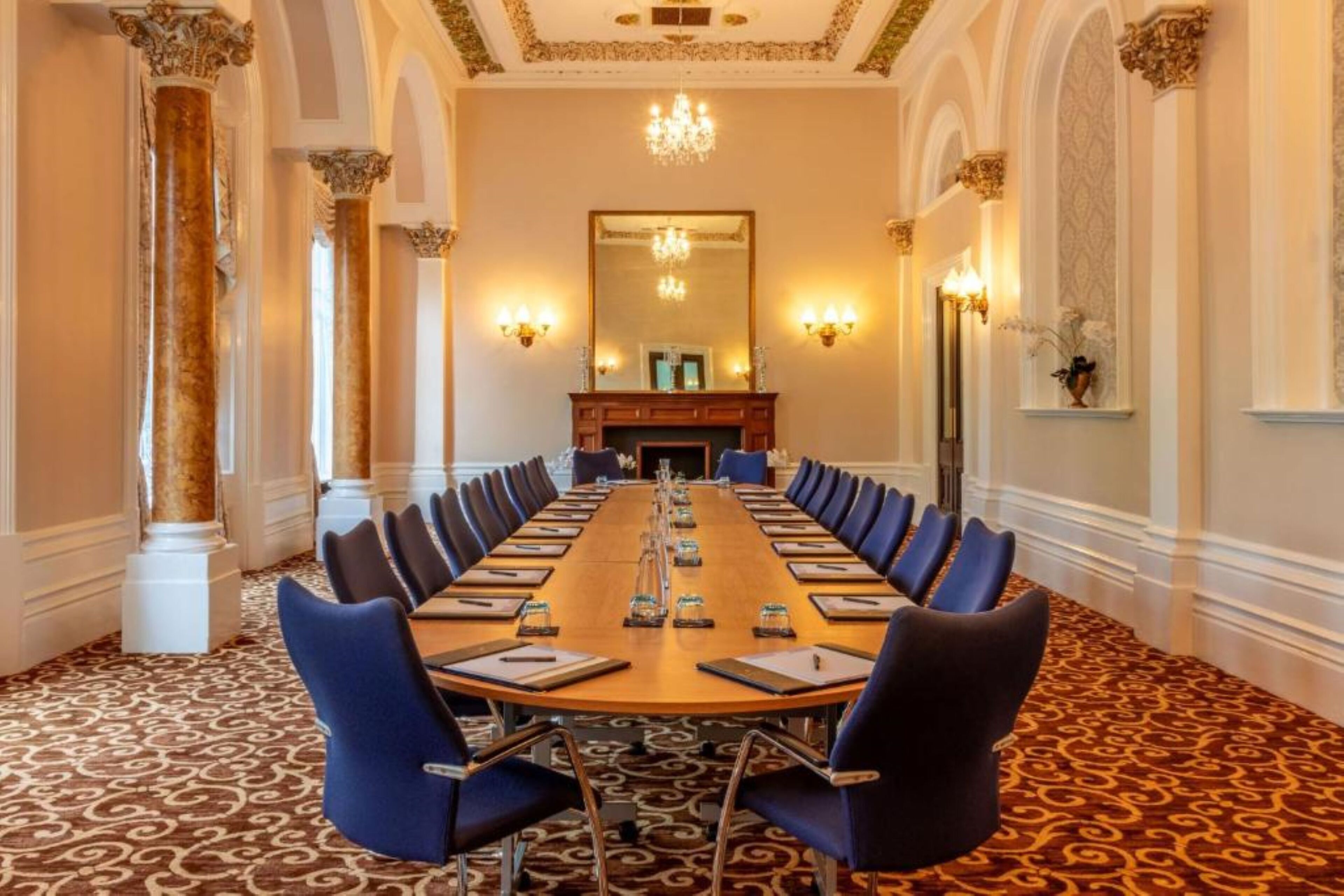 A conference room with a long table, blue chairs, and a chandelier.