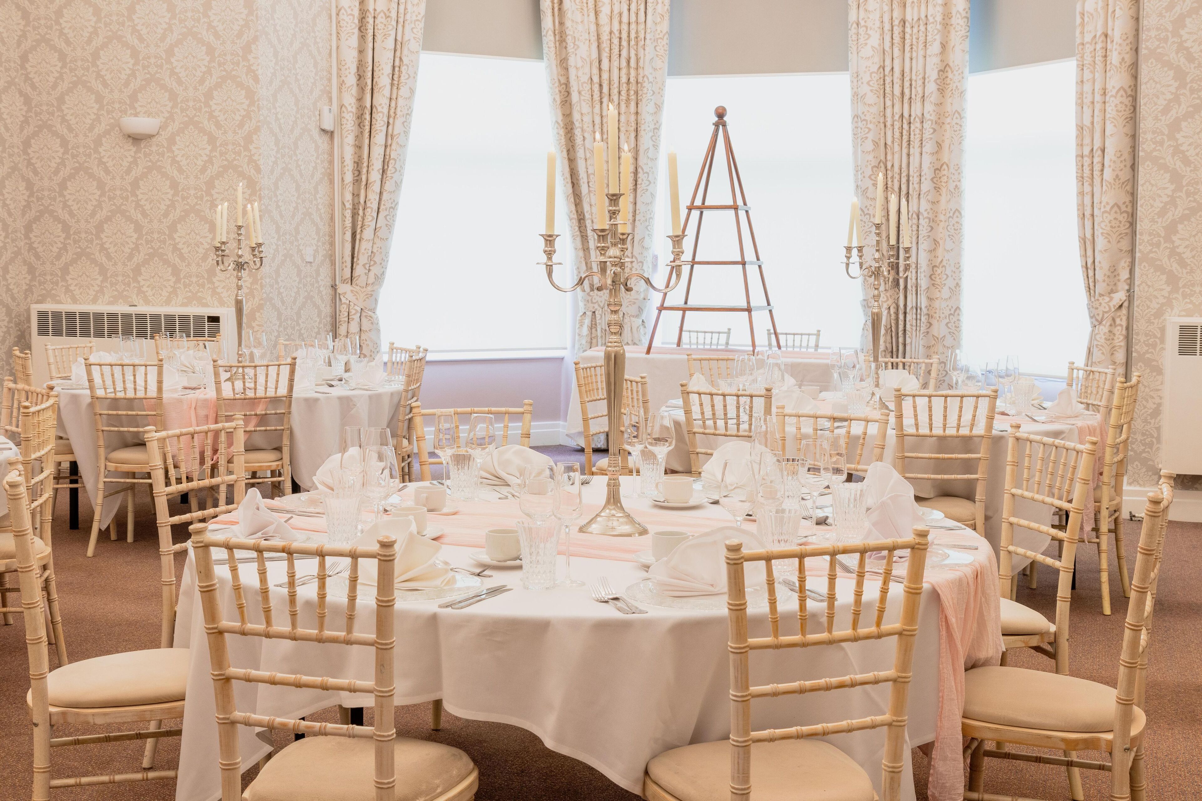 Une salle de banquet avec des tables rondes dressées pour le repas, agrémentée de nappes blanches et de chaises assorties.