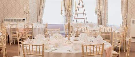 A banquet hall with round tables set for dining, featuring white tablecloths and matching chairs.