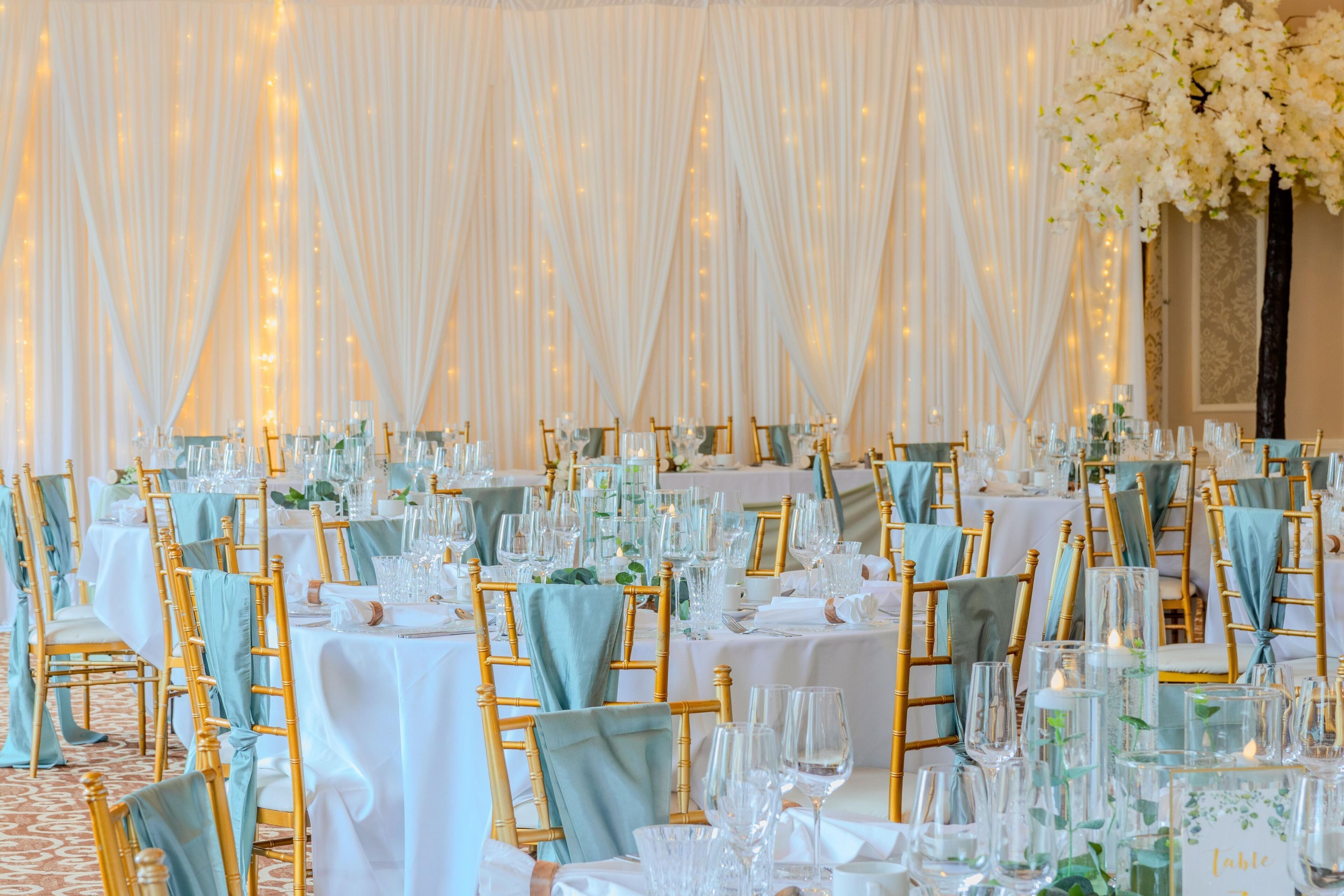 Un salón de banquetes con mesas redondas, sillas doradas y manteles blancos.
