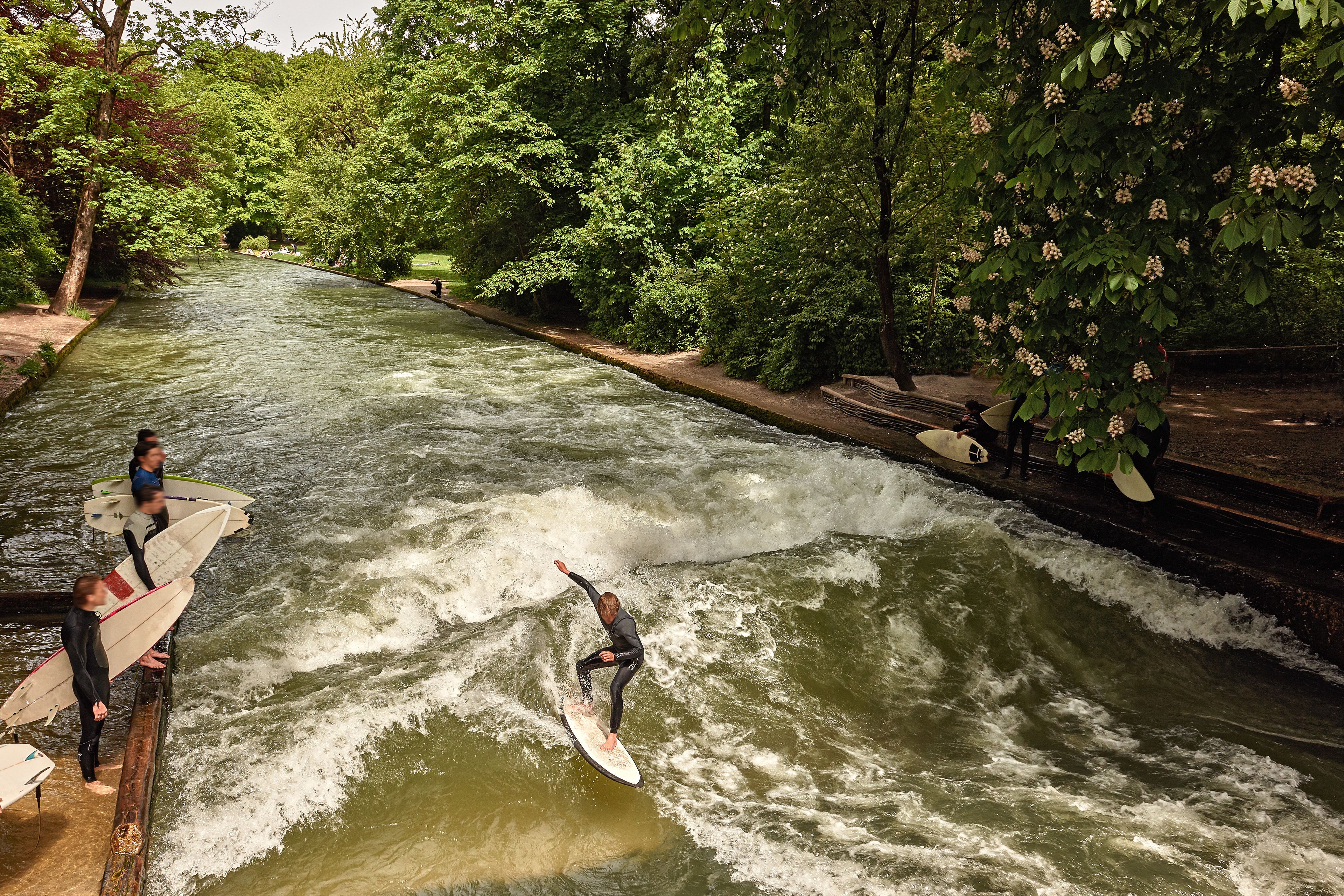 Een rivier met een persoon aan het surfen, omgeven door weelderige begroeiing.