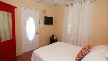 A bedroom with a bed, a red dresser, a ceiling fan, a TV, and a window with curtains.