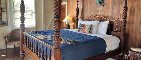 A four-poster bed with a blue bedspread, wooden headboard, and a ceiling fan.