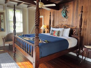 A four-poster bed with a blue bedspread, wooden headboard, and a ceiling fan. - Club Comanche Hotel, St. Croix (Christiansted)