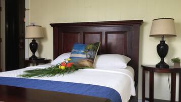 A neatly made bed with a blue and white bedspread, a decorative pillow with a beach scene, and a small bouquet of flowers. There are two bedside tables, each with a lamp and a small plant.